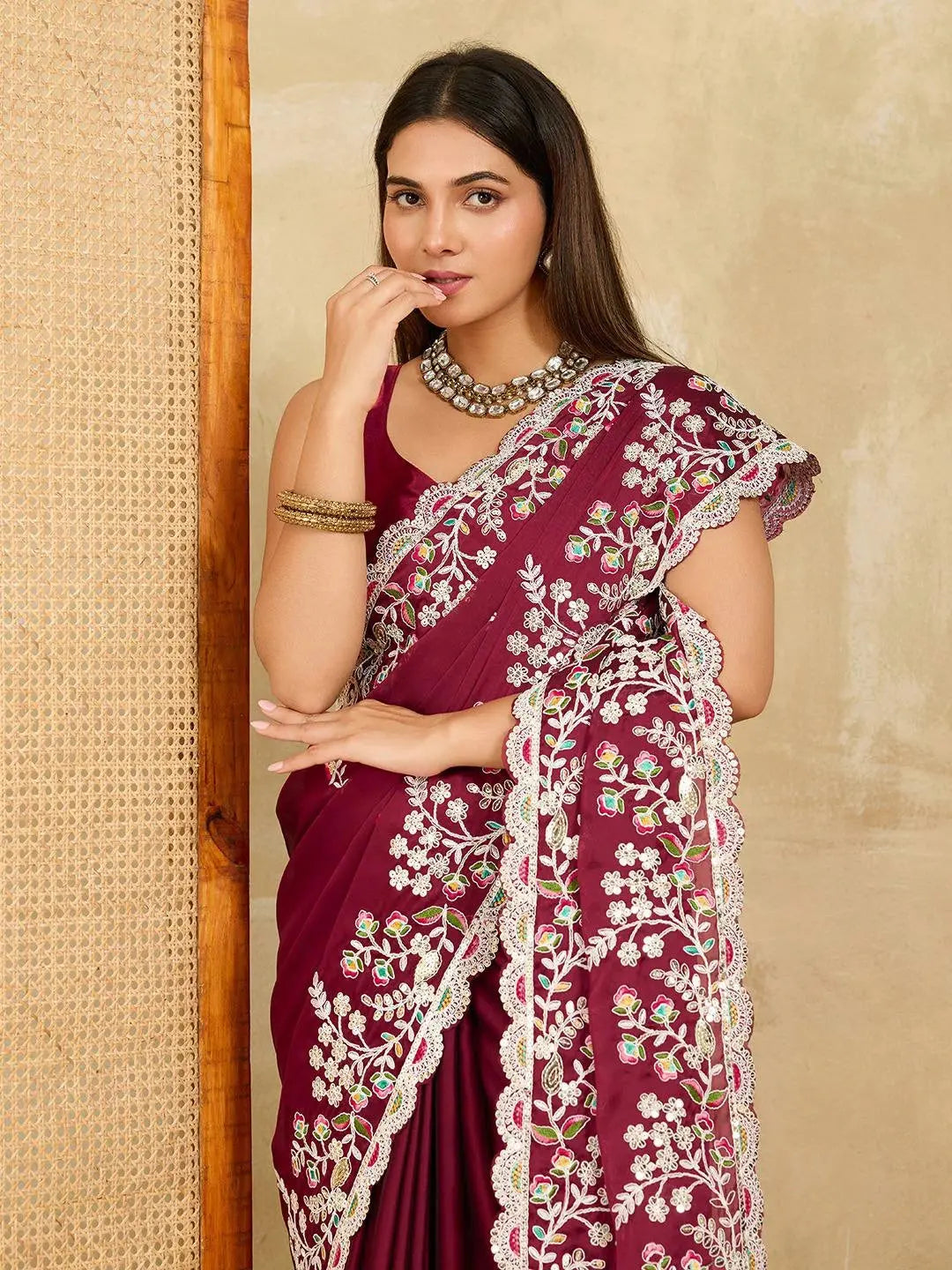 Woman wearing a maroon saree with white embroidery against a beige wall.
